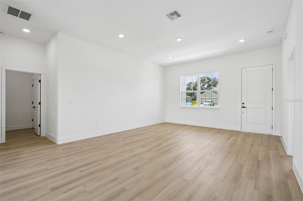An empty room with white walls, light wood-look flooring, recessed lighting, and a single window — 6207 SW 128TH STREET ROAD, OCALA, FL