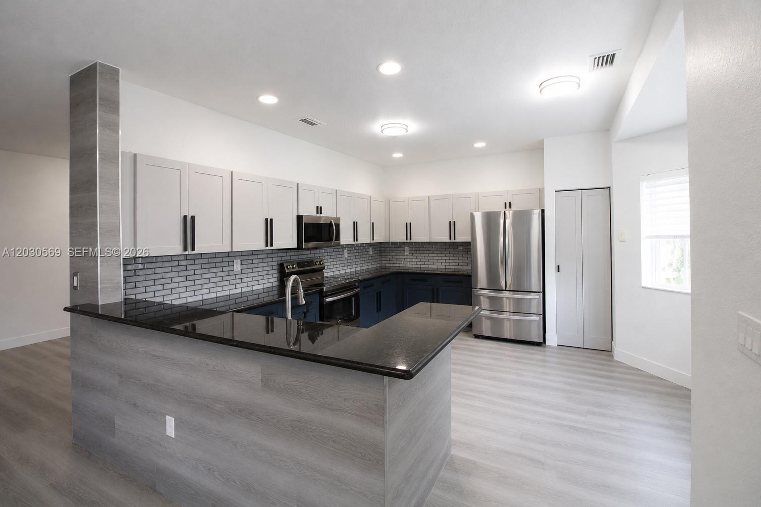 A kitchen features two-tone cabinets, a black countertop, and a gray wood-look peninsula — 2564 SW 147th Path, Miami FL 33185, MIAMI, FL