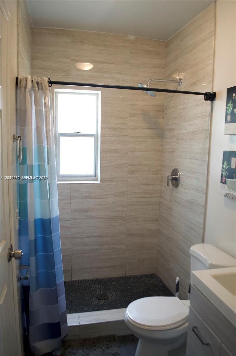 A bathroom features a tiled walk-in shower, a toilet, and a blue-patterned shower curtain — 5530 N Miami Ave # 2, Miami FL 33127, MIAMI, FL