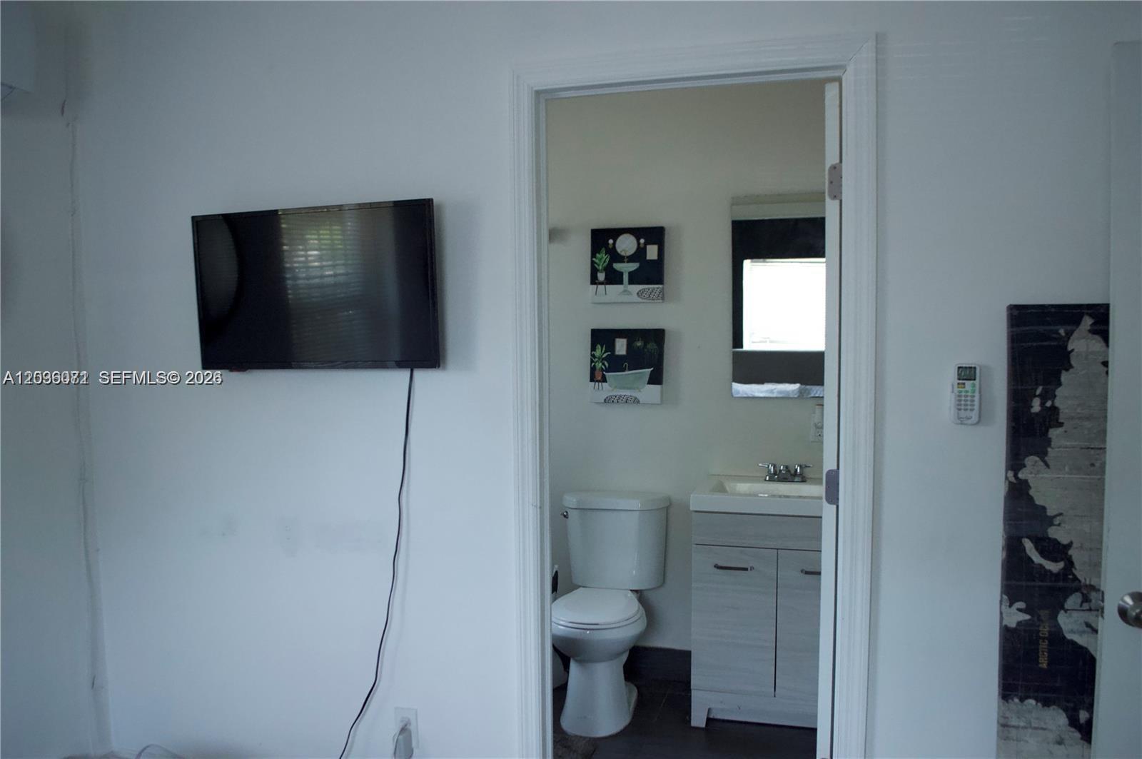 A wall-mounted television overlooks a doorway leading into a small bathroom with a vanity — 5530 N Miami Ave # 2, Miami FL 33127, MIAMI, FL