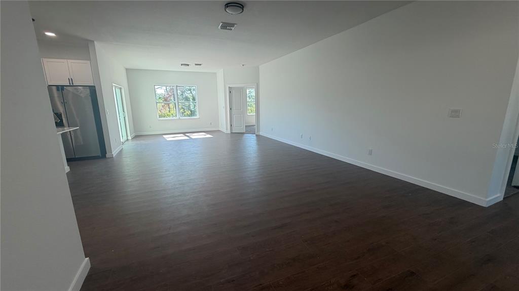 An open-concept living area features dark wood-look flooring, white walls, and a kitchen corner — 319 SPAULDING STREET, PORT CHARLOTTE, FL