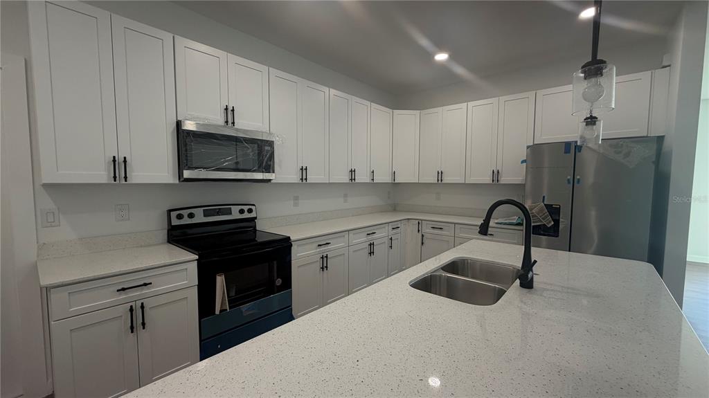 A modern kitchen features white cabinets, stainless steel appliances, and a large quartz-topped island — 319 SPAULDING STREET, PORT CHARLOTTE, FL