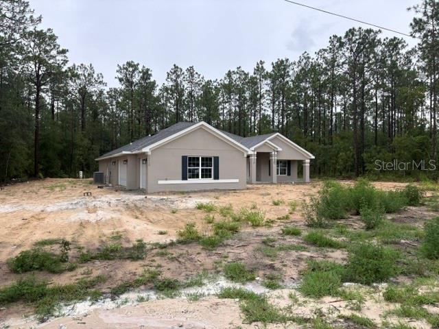 A newly constructed, single-story beige house sits on a sandy lot surrounded by pine trees — 13510 SW 64TH STREET ROAD, OCALA, FL