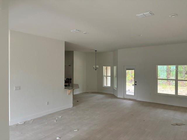 An open-concept living area with light-colored flooring, white walls, and a view of trees — 13510 SW 64TH STREET ROAD, OCALA, FL