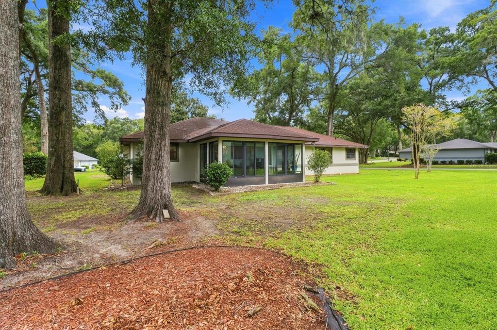 A single-story house with a screened-in porch sits on a large, grassy lot with trees — 9251 SW 192ND COURT, DUNNELLON, FL