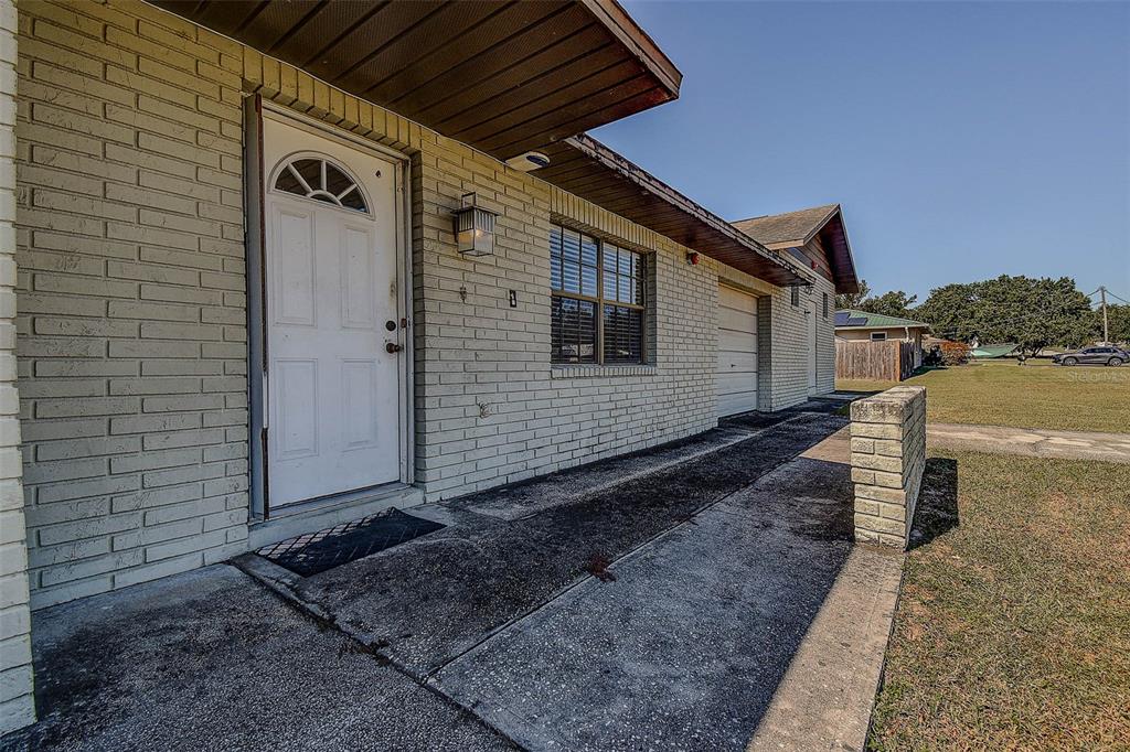 A side view of a light-colored brick house with a white door and concrete walkway — 11425 SUN ROAD, DADE CITY, FL