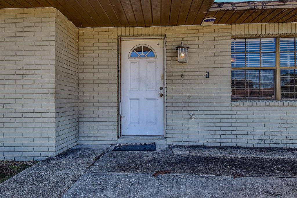 A white front door is centered on a beige brick exterior wall with a window — 11425 SUN ROAD, DADE CITY, FL