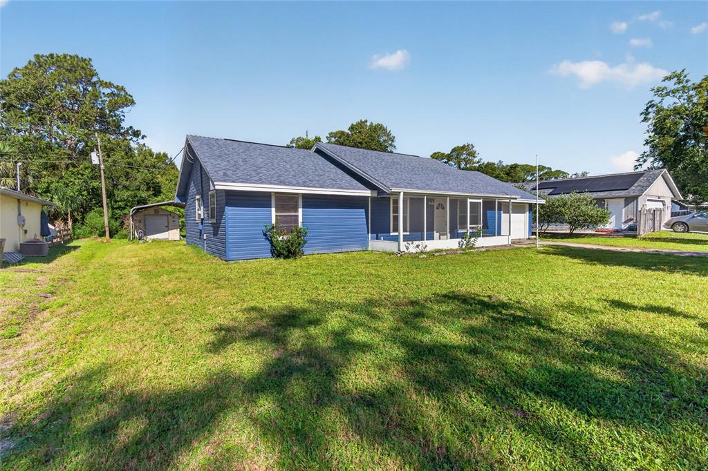 A blue house with a screened-in porch sits on a large grassy lot — 3012 UMBRELLA TREE DRIVE, EDGEWATER, FL
