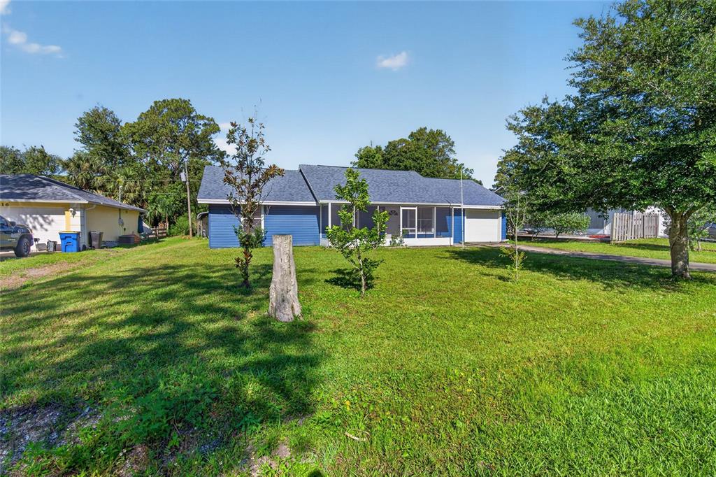 A blue single-story house with a shingled roof sits on a large, grassy lot — 3012 UMBRELLA TREE DRIVE, EDGEWATER, FL