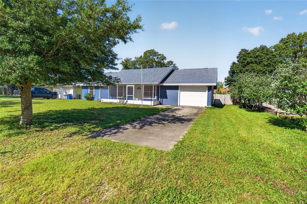 A single-story house with blue siding, a white garage door, and a concrete driveway — 3012 UMBRELLA TREE DRIVE, EDGEWATER, FL