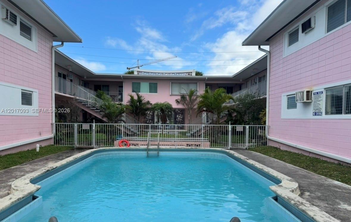 A rectangular swimming pool sits in the courtyard of a two-story pink apartment building — NORTH BAY VILLAGE, FL