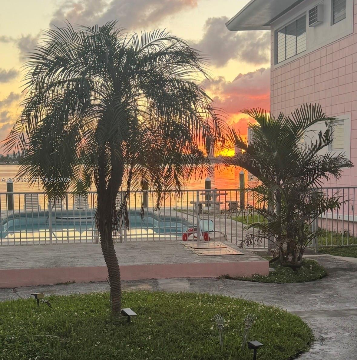 A swimming pool sits beside a pink building and palm trees at sunset — NORTH BAY VILLAGE, FL