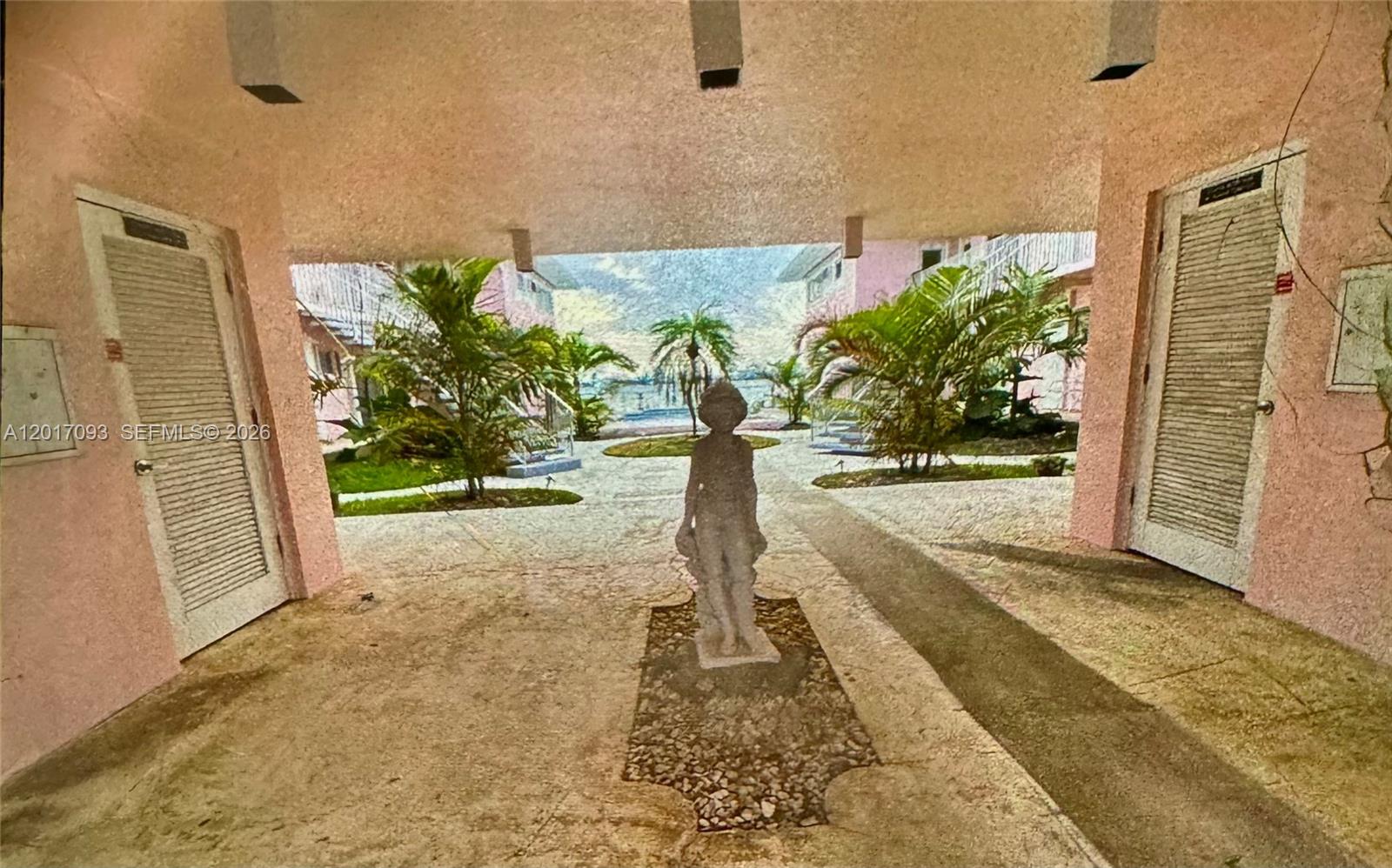 A statue stands in a covered walkway between two pink buildings with louvered doors — NORTH BAY VILLAGE, FL