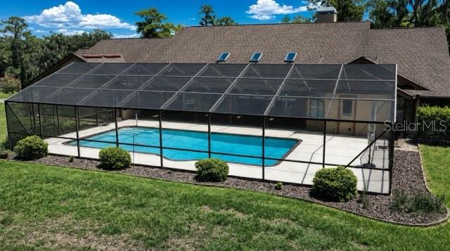 A screened-in swimming pool sits behind a large house with a brown shingled roof — 5950 SW 21ST AVENUE ROAD, OCALA, FL