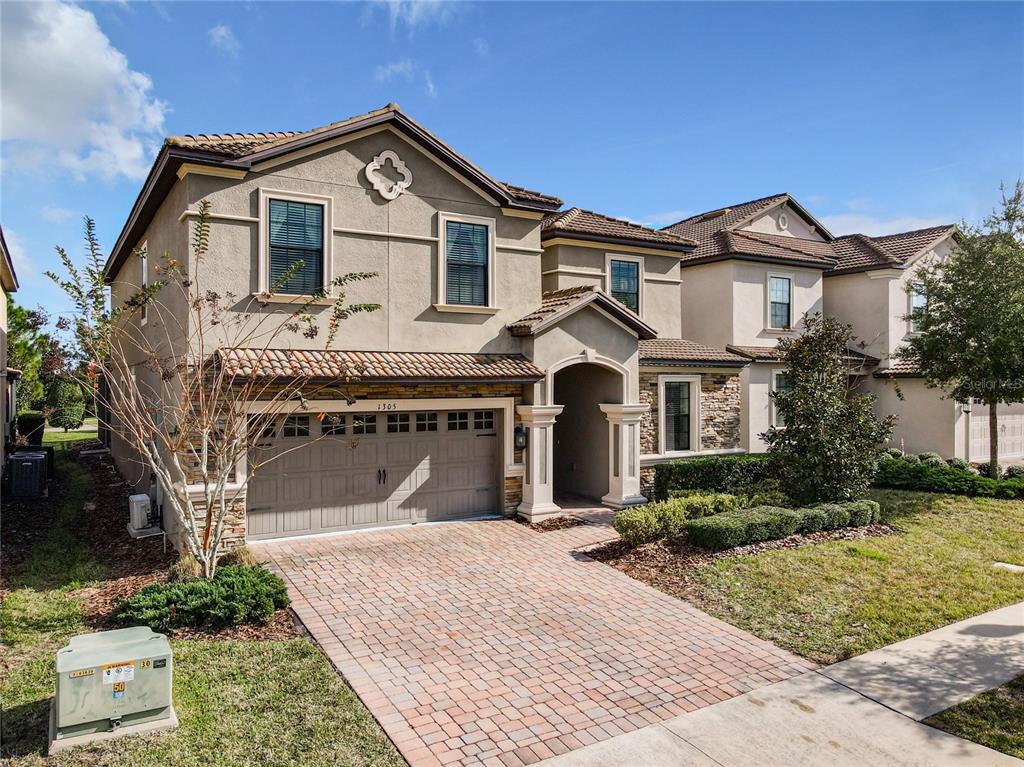 A two-story suburban house with a tan stucco exterior, stone accents, and a brick driveway — 1305 DIVOT WAY, DAVENPORT, FL