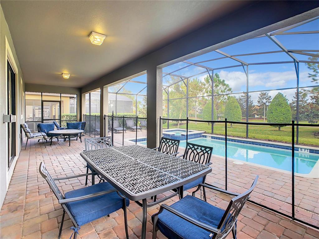 A covered patio features a dining set, pool safety fence, and a view of the pool — 1305 DIVOT WAY, DAVENPORT, FL