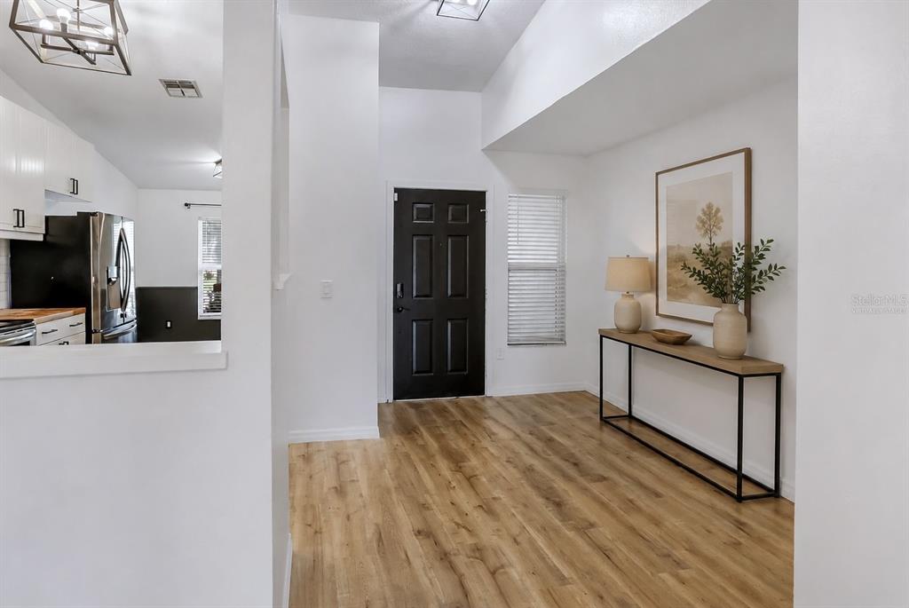An entryway with wood-look flooring, a black front door, and a console table against the wall — 1107 COVINGTON STREET, OVIEDO, FL