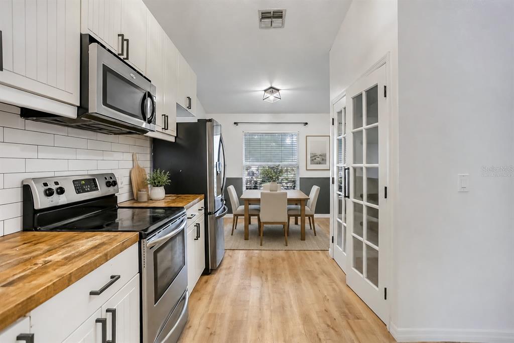 A kitchen with white cabinets, wood countertops, and stainless steel appliances leads to a dining area — 1107 COVINGTON STREET, OVIEDO, FL