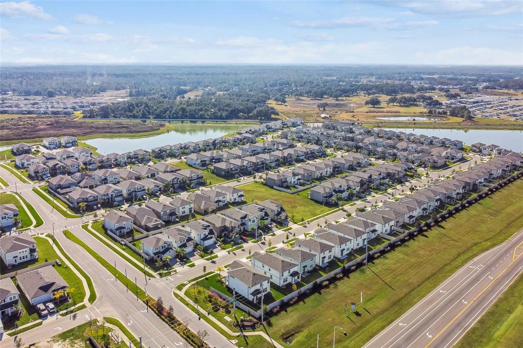 An aerial view shows a suburban neighborhood with many houses surrounding a central lake — 3303 FALL HARVEST DRIVE, ZEPHYRHILLS, FL
