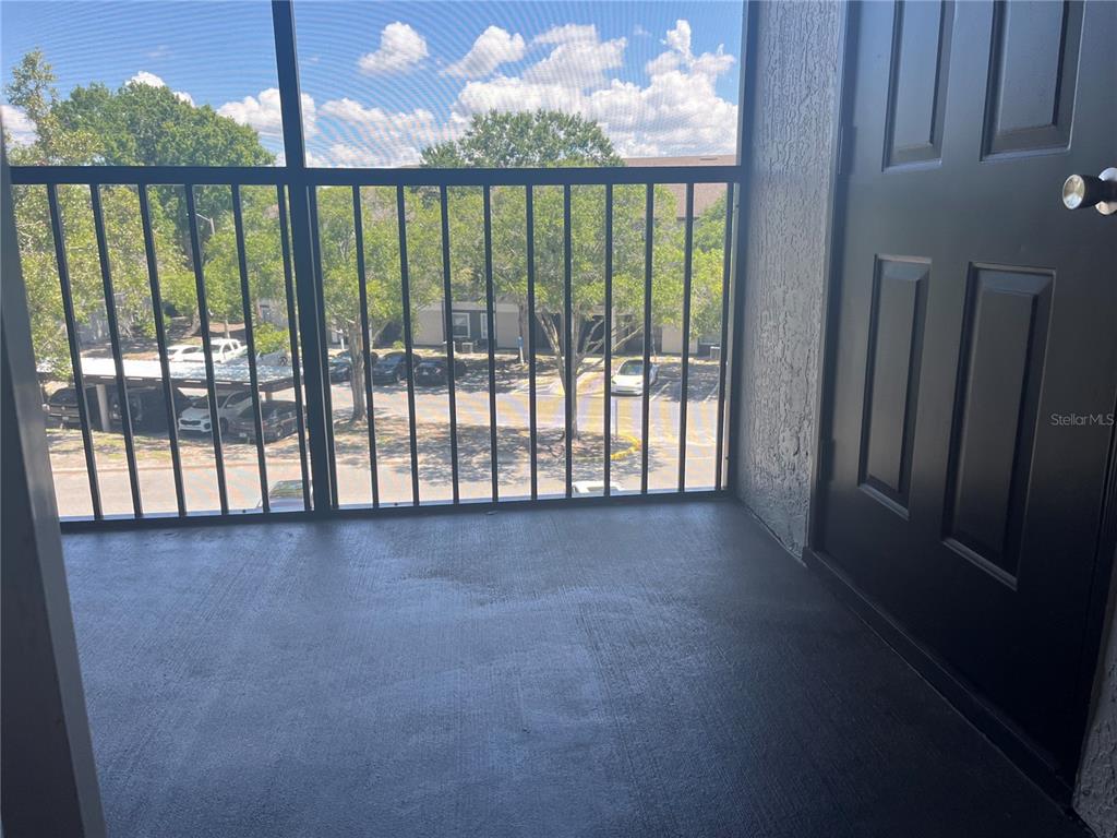A screened-in balcony with a concrete floor overlooks a parking lot and trees — 7511 SEURAT STREET UNIT 10304, ORLANDO, FL