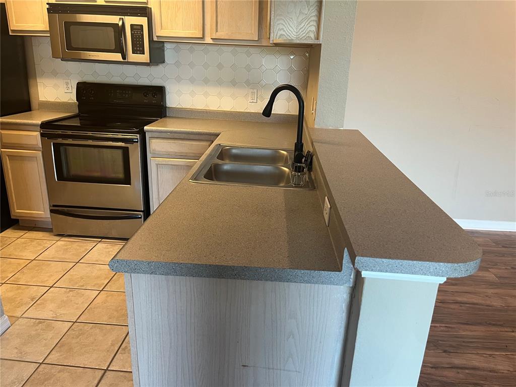A kitchen features light wood cabinets, a stainless steel stove, and a gray countertop — 7511 SEURAT STREET UNIT 10304, ORLANDO, FL