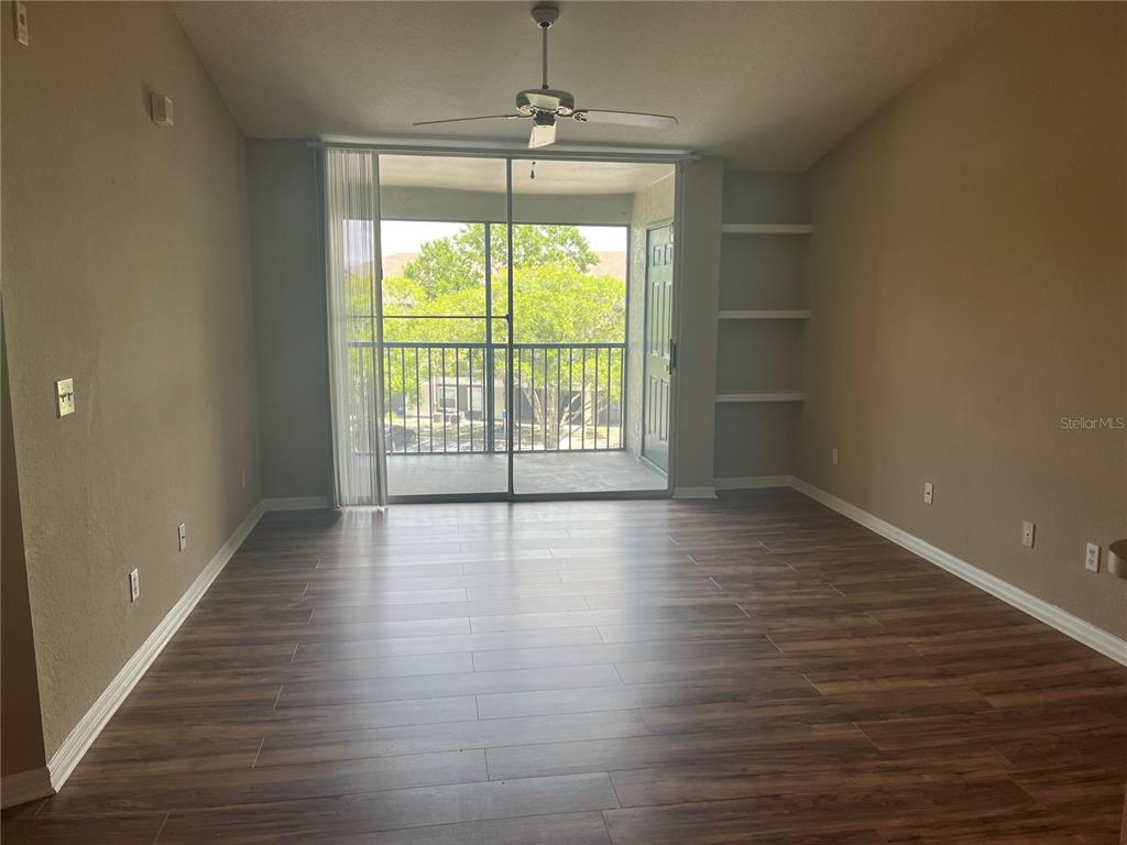 An empty living room features wood-look flooring, a ceiling fan, built-in shelves, and a balcony — 7511 SEURAT STREET UNIT 10304, ORLANDO, FL