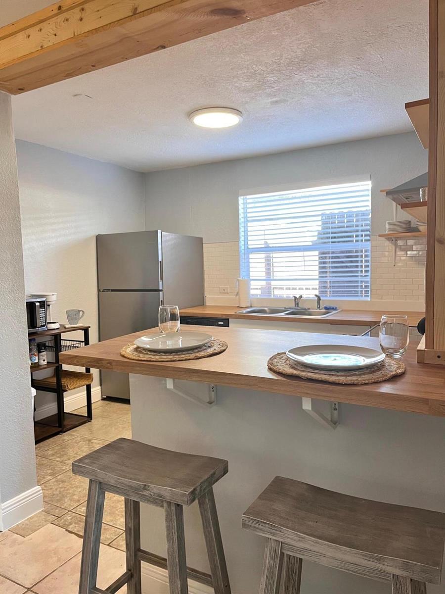 A kitchen features a wooden breakfast bar with two stools, stainless steel appliances, and shelving — 118 SW 12th Avenue, Delray Beach FL 33444, DELRAY BEACH, FL
