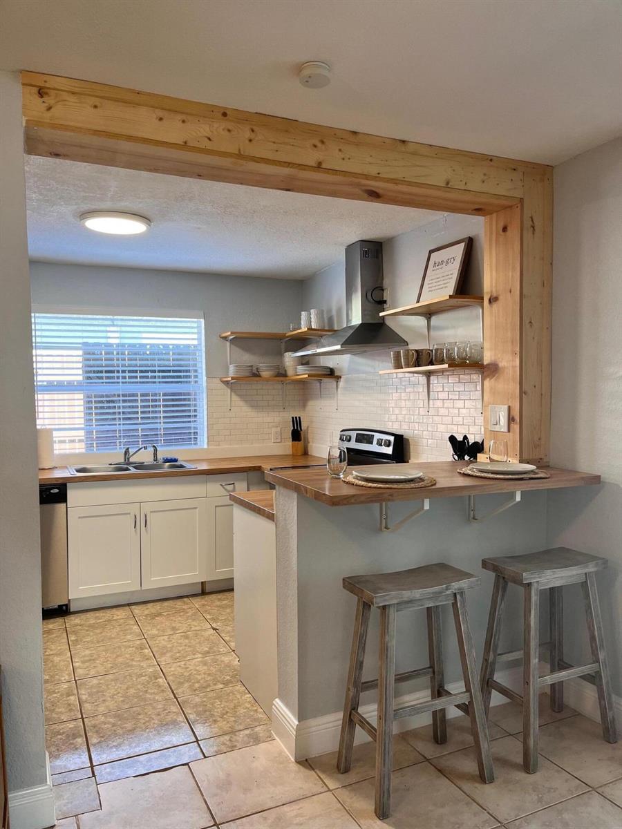 A kitchen features white cabinets, wood countertops, open shelving, and a breakfast bar with stools — 118 SW 12th Avenue, Delray Beach FL 33444, DELRAY BEACH, FL