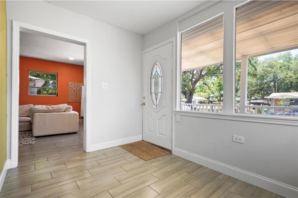 An entryway with light wood-look tile flooring, a white front door, and a view into a living room — 2821 MARCONI STREET, TAMPA, FL