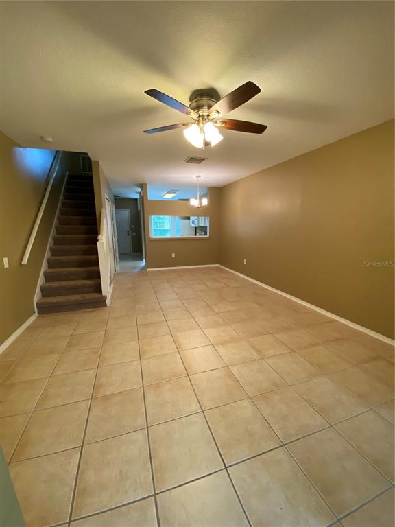 An open-concept room features beige tile flooring, tan walls, a ceiling fan, and carpeted stairs — 1309 THROCKMORTON DRIVE, WESLEY CHAPEL, FL