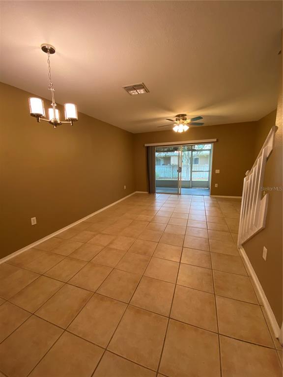 An open living area features tan tile flooring, a chandelier, and sliding glass patio doors — 1309 THROCKMORTON DRIVE, WESLEY CHAPEL, FL