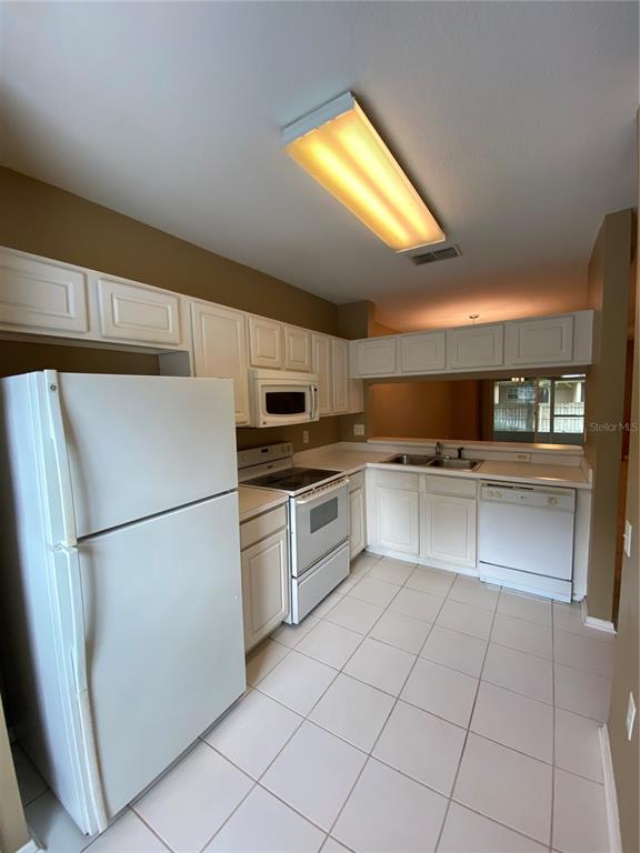 A kitchen features white cabinets, white appliances, tiled floors, and a pass-through window — 1309 THROCKMORTON DRIVE, WESLEY CHAPEL, FL