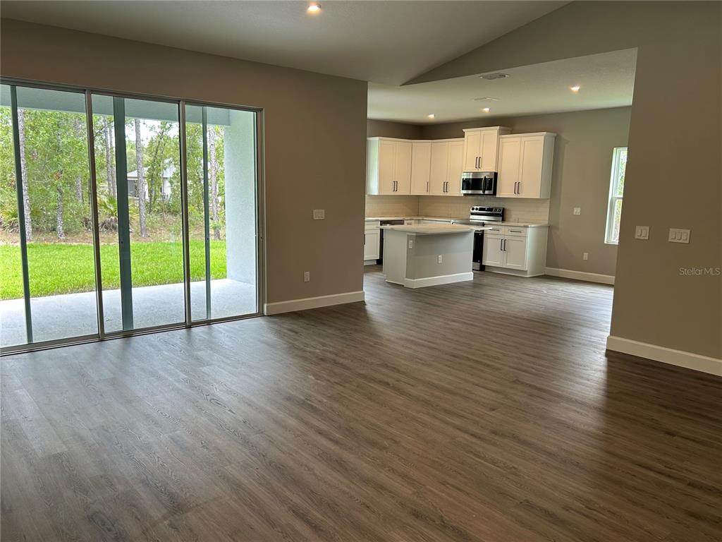 An open-concept kitchen with white cabinets and an island overlooks a living area with sliding doors — 13190 ENGLISH FIR COURT, BROOKSVILLE, FL