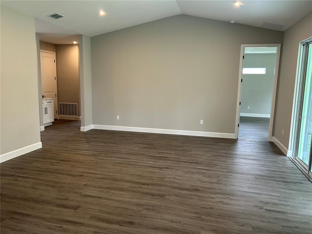 An empty room with wood-look flooring, a vaulted ceiling, and a doorway leading to another room — 13190 ENGLISH FIR COURT, BROOKSVILLE, FL