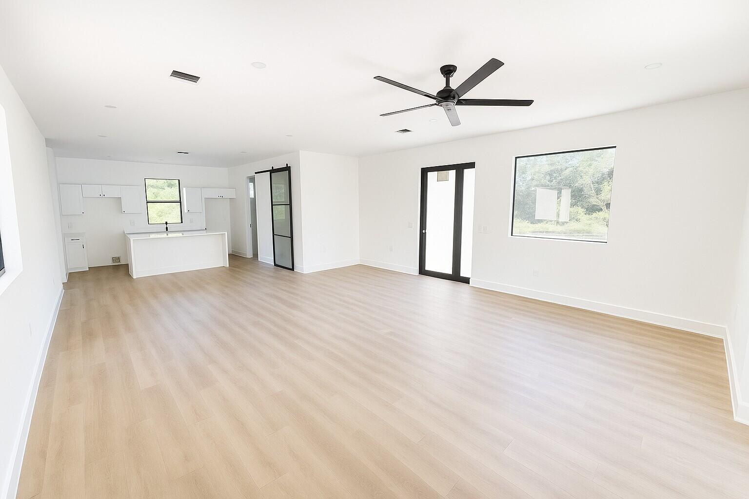 An open-concept living area features light wood floors, white walls, and a modern kitchen — 1034 E Alcalde St Street E, Lehigh Acres FL 33974, LEHIGH ACRES, FL