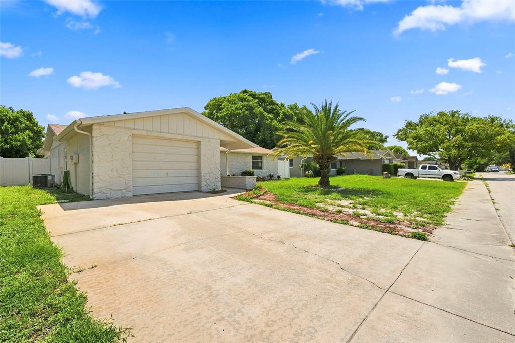 A single-story house with a white stone facade, a garage, and a palm tree — 8936 WINDSONG LANE, PORT RICHEY, FL