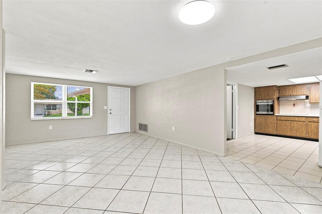 An open-concept living area with light-colored tile flooring leads into a kitchen with wood cabinets — 8936 WINDSONG LANE, PORT RICHEY, FL