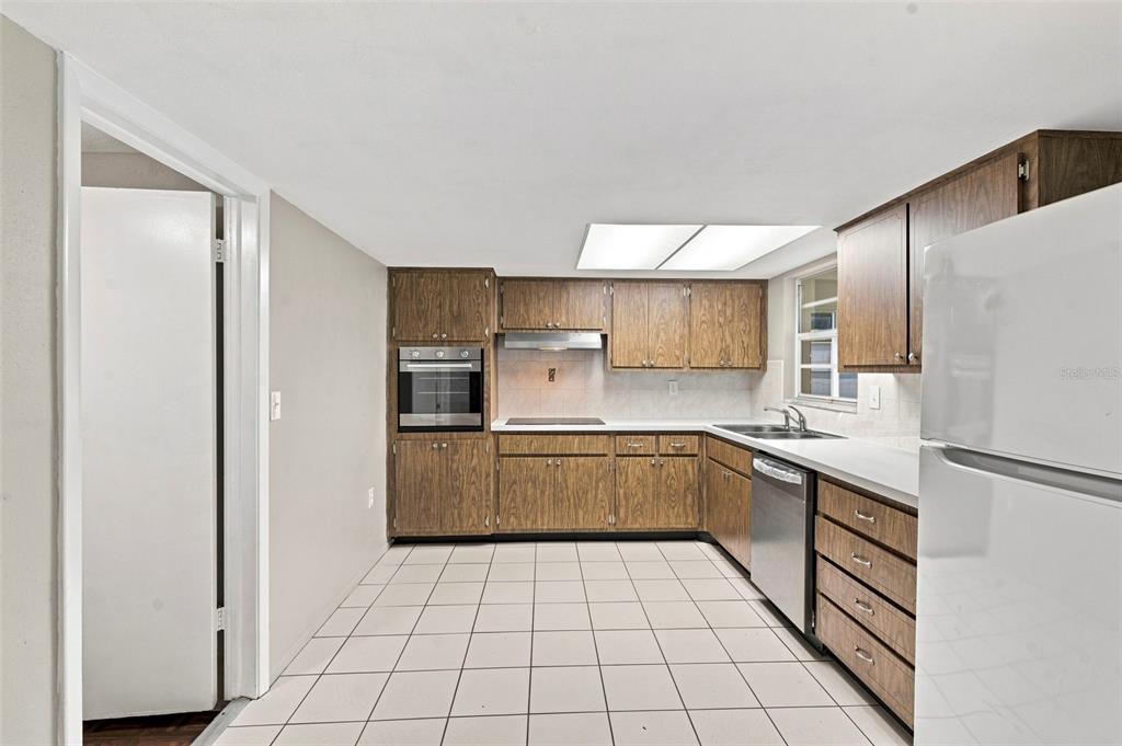 A kitchen features wood-grain cabinets, white tile flooring, a built-in oven, and white appliances — 8936 WINDSONG LANE, PORT RICHEY, FL