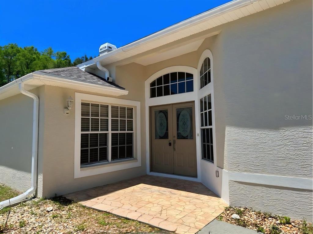 The exterior of a house features a tan stucco facade, double front doors, and a porch — 10104 BEEFMASTER COURT, NEW PORT RICHEY, FL
