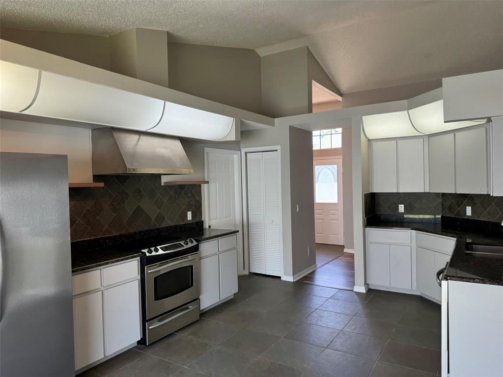 A kitchen features white cabinets, dark granite countertops, stainless steel appliances, and tiled flooring — 10104 BEEFMASTER COURT, NEW PORT RICHEY, FL