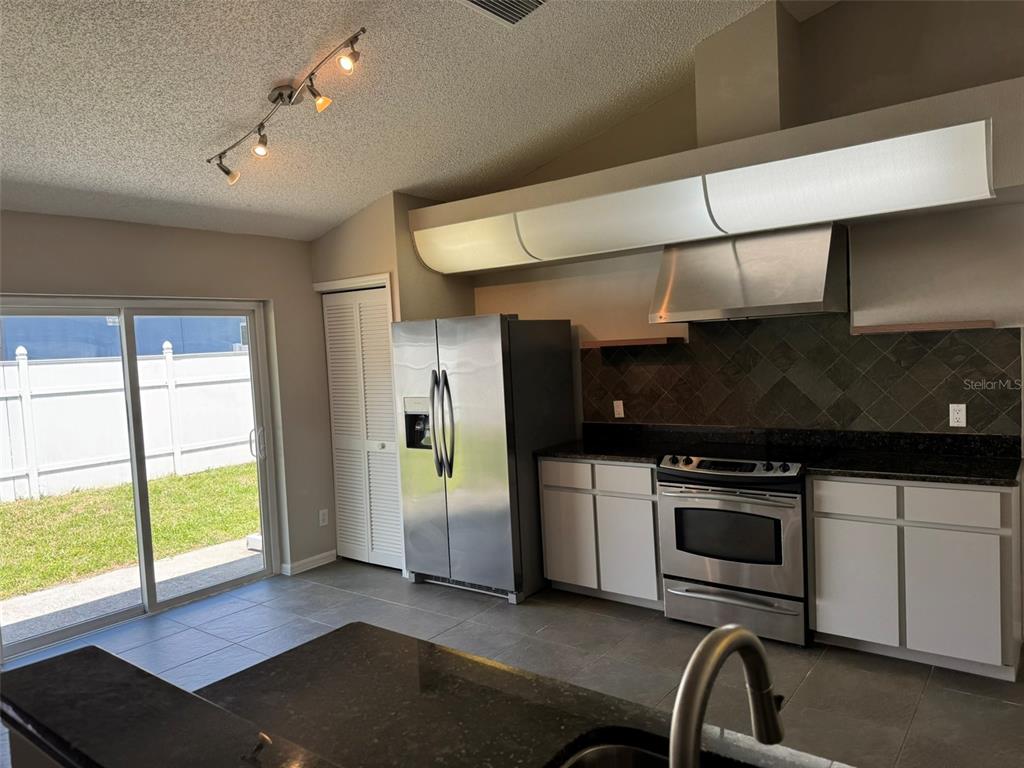 A kitchen features white cabinets, dark granite countertops, stainless steel appliances, and a sliding door — 10104 BEEFMASTER COURT, NEW PORT RICHEY, FL