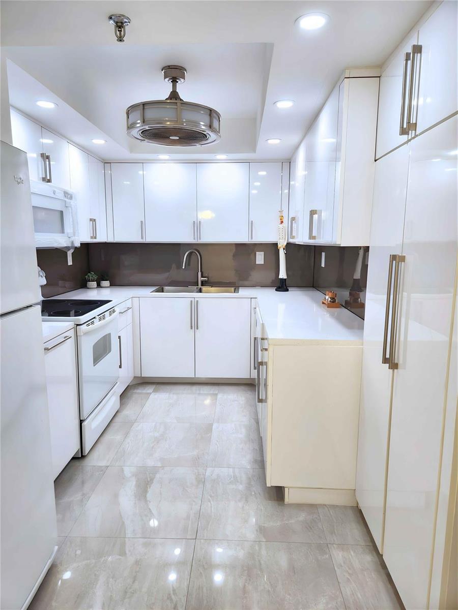A white kitchen features glossy cabinets, a brown backsplash, and light-colored tiled flooring — 6463 La Costa Drive # 301, Boca Raton FL 33433, BOCA RATON, FL