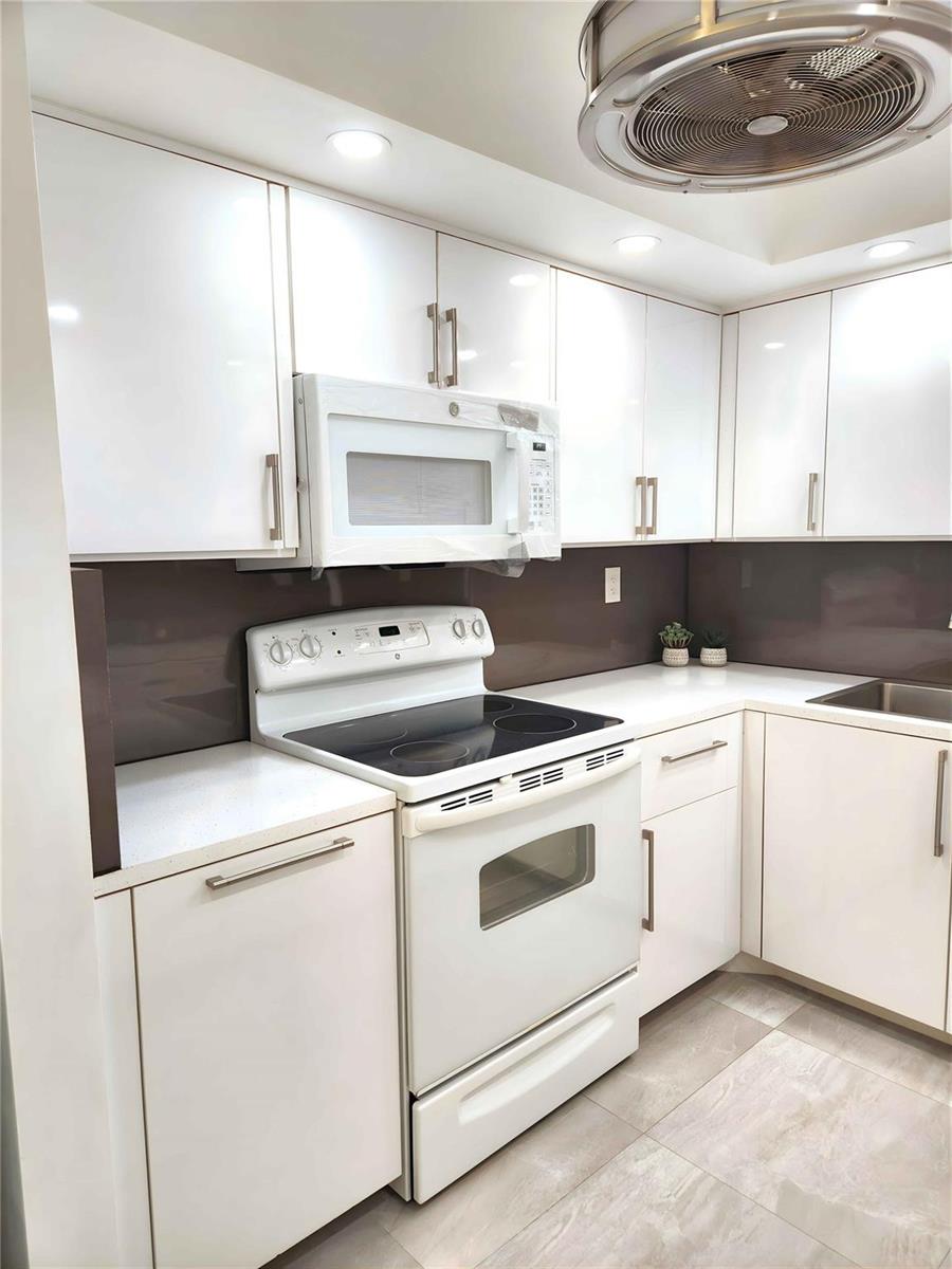 A kitchen features white cabinets, a white electric range, and a dark brown backsplash — 6463 La Costa Drive # 301, Boca Raton FL 33433, BOCA RATON, FL