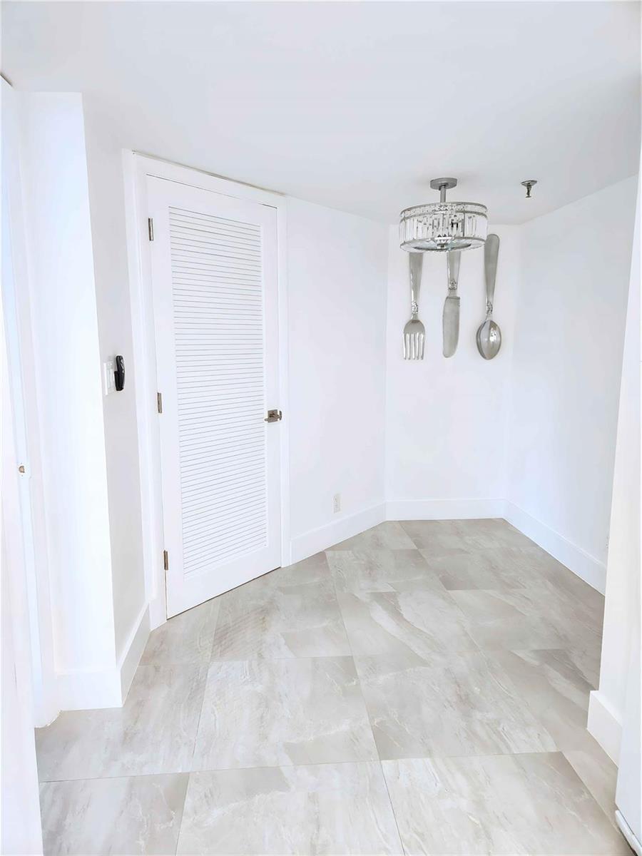 A small, white-walled dining nook features light-colored tile flooring and oversized wall-mounted cutlery decor — 6463 La Costa Drive # 301, Boca Raton FL 33433, BOCA RATON, FL