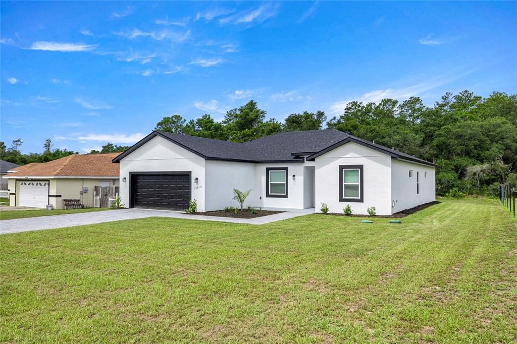 A white, single-story house with a black garage door and roof sits on a lawn — 15610 SW 28TH AVENUE ROAD, OCALA, FL