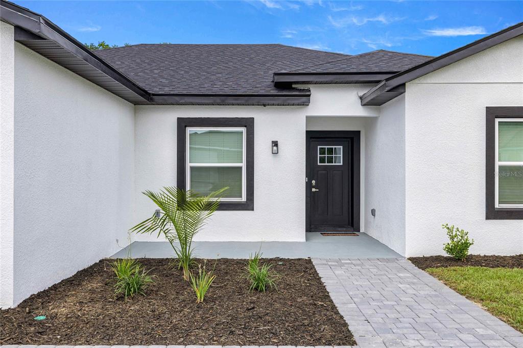 A white stucco house exterior features a black front door and a gray paver walkway — 15610 SW 28TH AVENUE ROAD, OCALA, FL