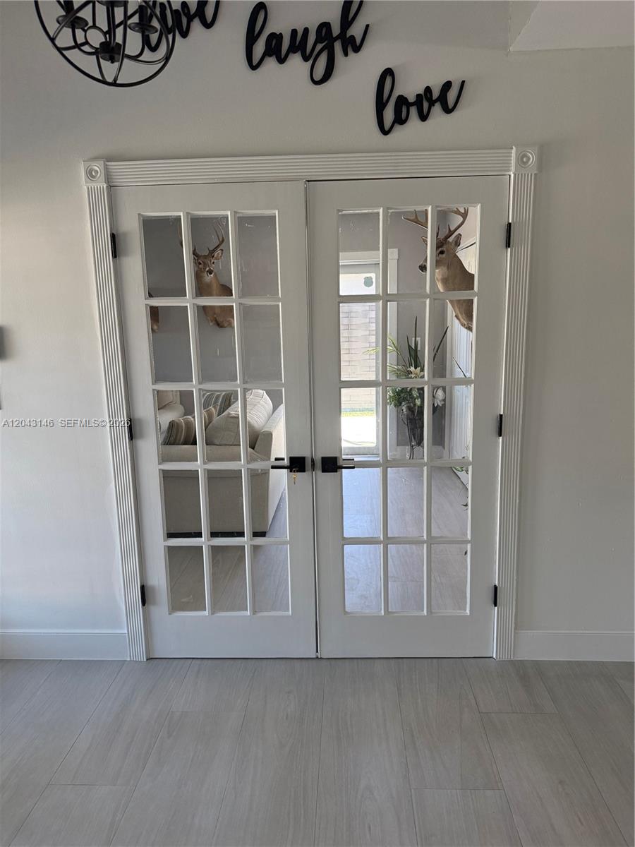 A light-colored dog stands on wood-look tile flooring in a dining area with French doors — 4947 SW 143rd Ave, Miami FL 33175, MIAMI, FL
