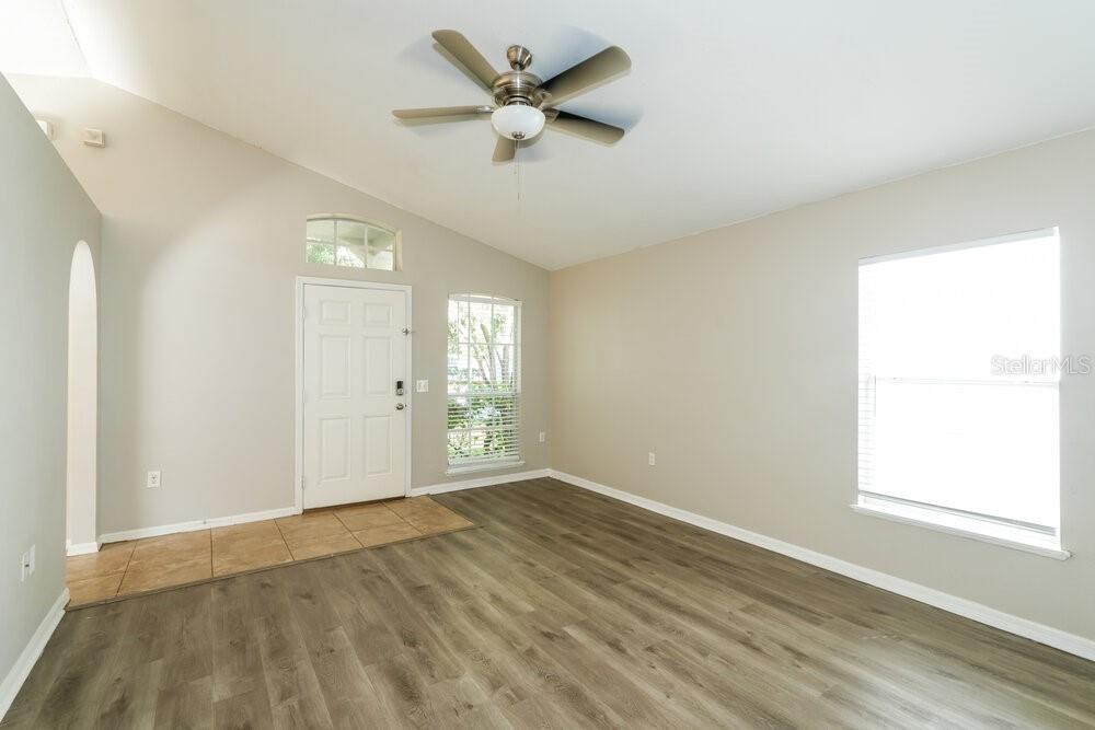 An empty living room features a vaulted ceiling, a ceiling fan, and wood-look flooring — 17031 ONGAR COURT, LAND O LAKES, FL
