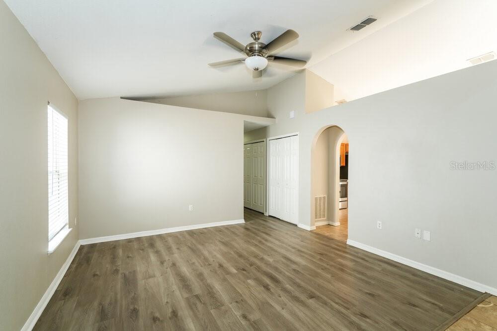 An empty living room with wood-look flooring, a vaulted ceiling, and a ceiling fan — 17031 ONGAR COURT, LAND O LAKES, FL