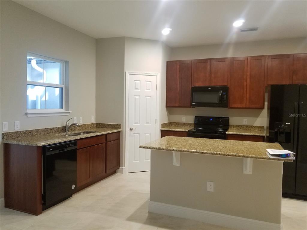 A kitchen features dark wood cabinets, granite countertops, black appliances, and a central island — 8504 MAGNIFICENT LANE, GROVELAND, FL